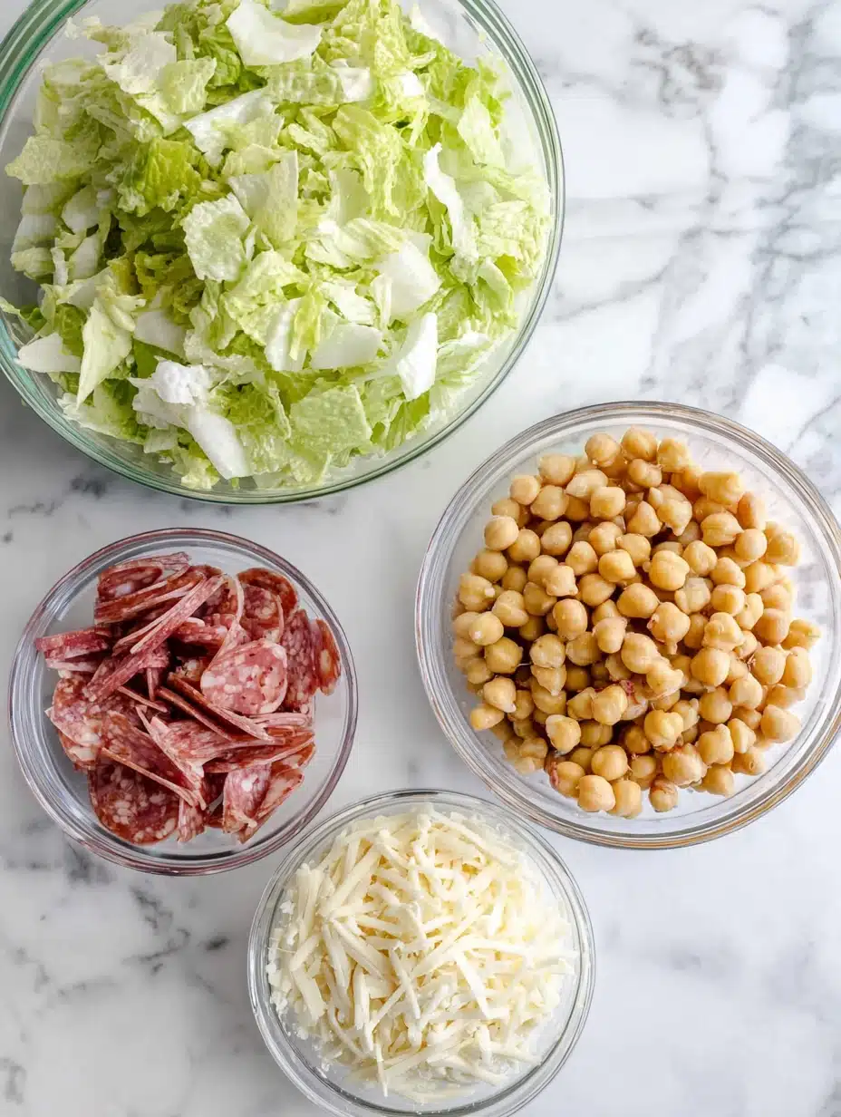 Overhead flat lay of copycat La Scala Chopped Salad ingredients in glass bowls on white marble.
