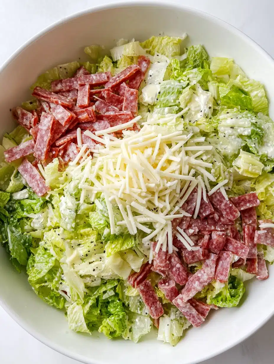 Copycat La Scala Chopped Salad with lettuce, salami, and mozzarella layered in a white bowl before mixing.