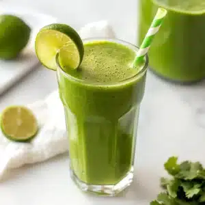 Sugar detox smoothie in a clear glass with lime and cilantro on marble background