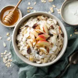 Top-down view of a creamy Bircher Muesli recipe in a white bowl with yogurt, grated apple, and almonds.