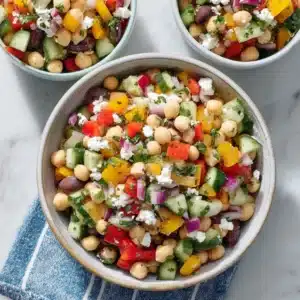 Colorful dense bean salad in bowls with chickpeas, bell peppers, cucumber, feta cheese, and herbs on marble background