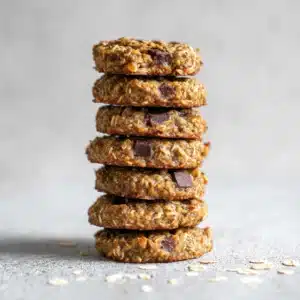 Stack of seven homemade oatmeal chia cookies with oats, dates, and dark chocolate on a light gray background.