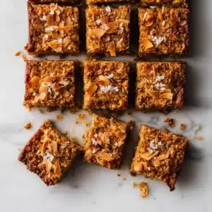 Peanut butter oat breakfast bars topped with toasted coconut flakes and sea salt on marble background