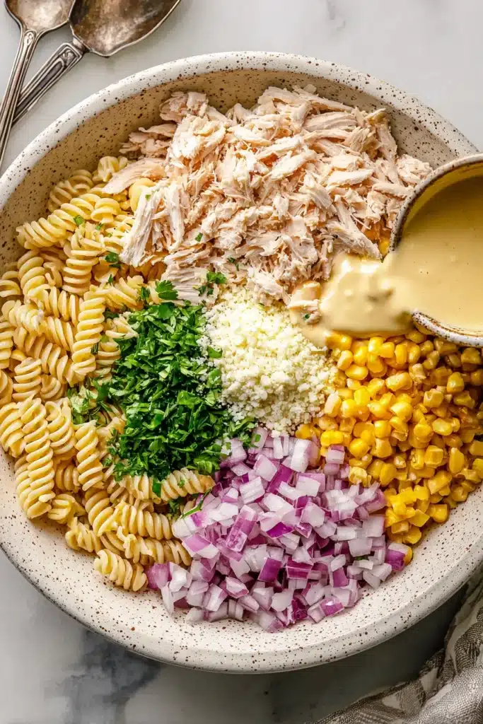 Unmixed Street Corn Pasta Salad ingredients in white bowl with dressing being poured