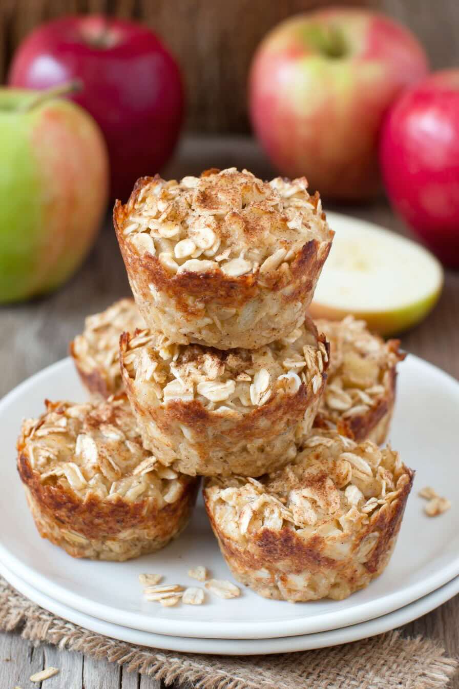 Baked oatmeal cups stacked on a plate with apples behind