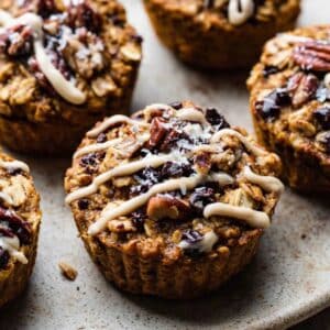 Pumpkin baked oatmeal cups topped with cranberries, pecans, and maple glaze