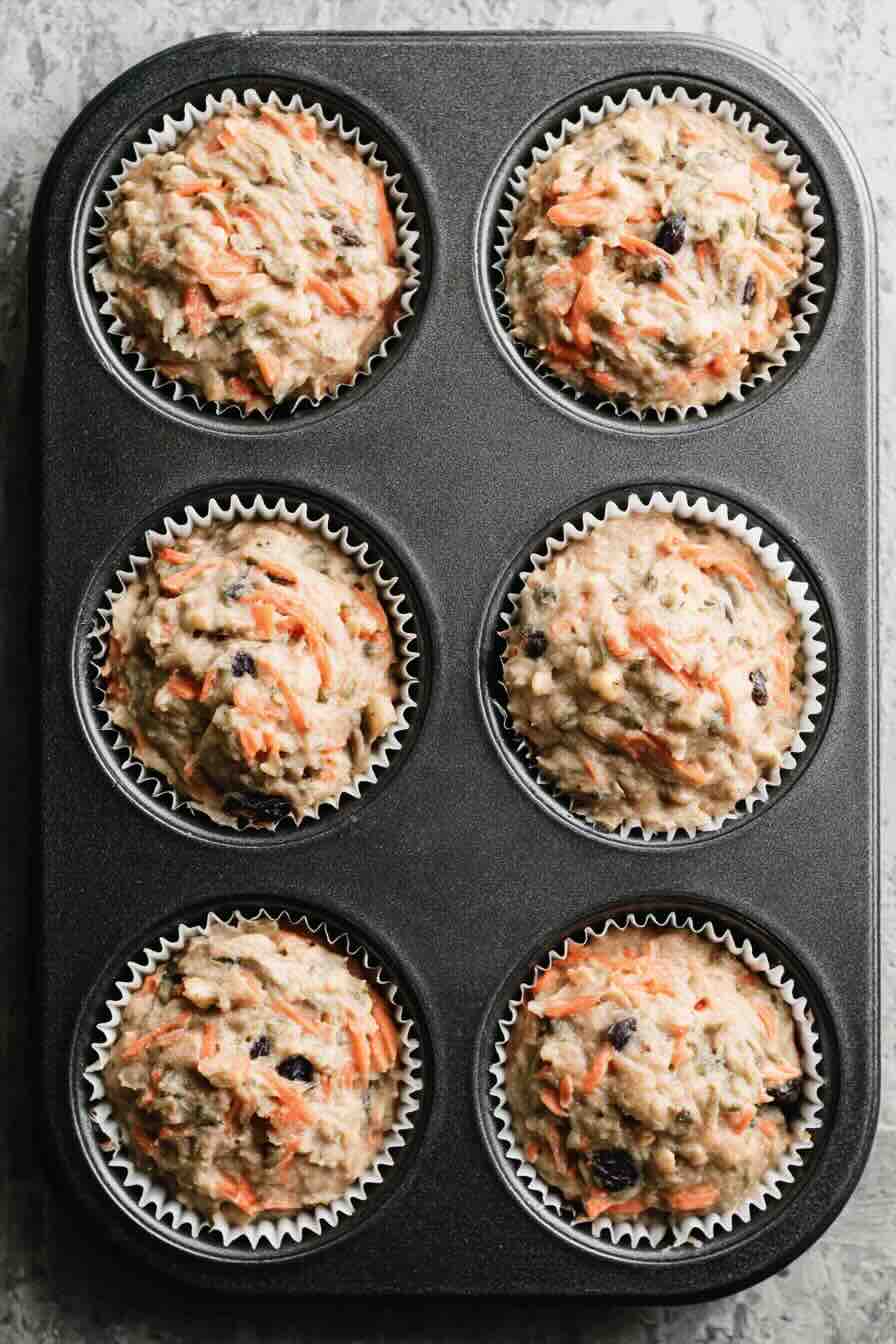 Raw Morning Glory Muffin batter in tin with shredded carrots and raisins