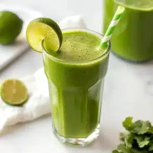 Pineapple ginger smoothie in a tall glass with a lime slice and green striped straw.
